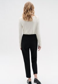 Lichtbeige sweater met lange mouwen, gecombineerd met op maat gemaakte zwarte broek. De broek heeft een gladde textuur en twee achterzakken.