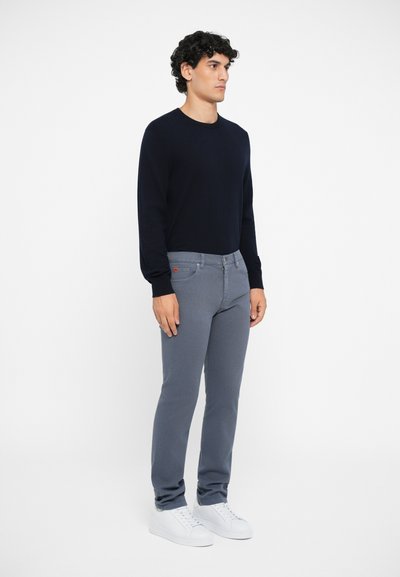 Gray jeans with a slim fit, topped with a navy sweater. Both are made from soft fabrics. White sneakers complete the outfit.