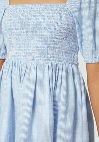Blau-weiß gestreiftes Kleid mit gerafftem Oberteil und kurzen Puffärmel, das einen weit schwingenden Rock aus leichtem Stoff hat.