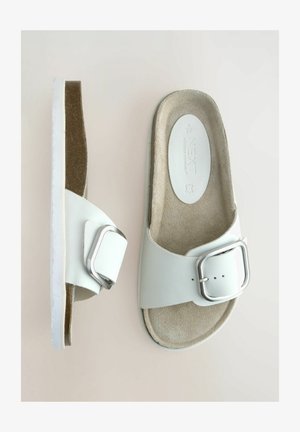 Valged slaidisandaalid, mis on valmistatud sünteetilisest materjalist, laia rihmaga, millel on hõbedane pannal, tekstureeritud tallaga ja lame tallaosa.