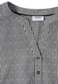 Gros plan sur le col d'une chemise à rayures verticales noires et blanches avec deux boutons noirs sous un décolleté en V avec étiquette de marque "CECIL".
