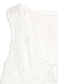 Witte geborduurde top met bloemen en een diepe V-hals, zachte textuur, verstelbare striksluiting en delicate bladrandpatronen op de stof.