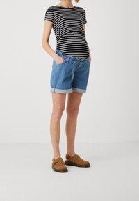 Randig svart och vit tight topp i kombination med denimshorts med avslappnad passform, uppvikta ärmar och elastisk midja. Bruna slip-on skor.