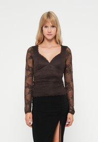 Donkerbruin blouse met lange mouwen en kantdetails, V-hals, getailleerde lijfje en gerimpelde textuur, gecombineerd met een zwarte rok met een zijsplit.