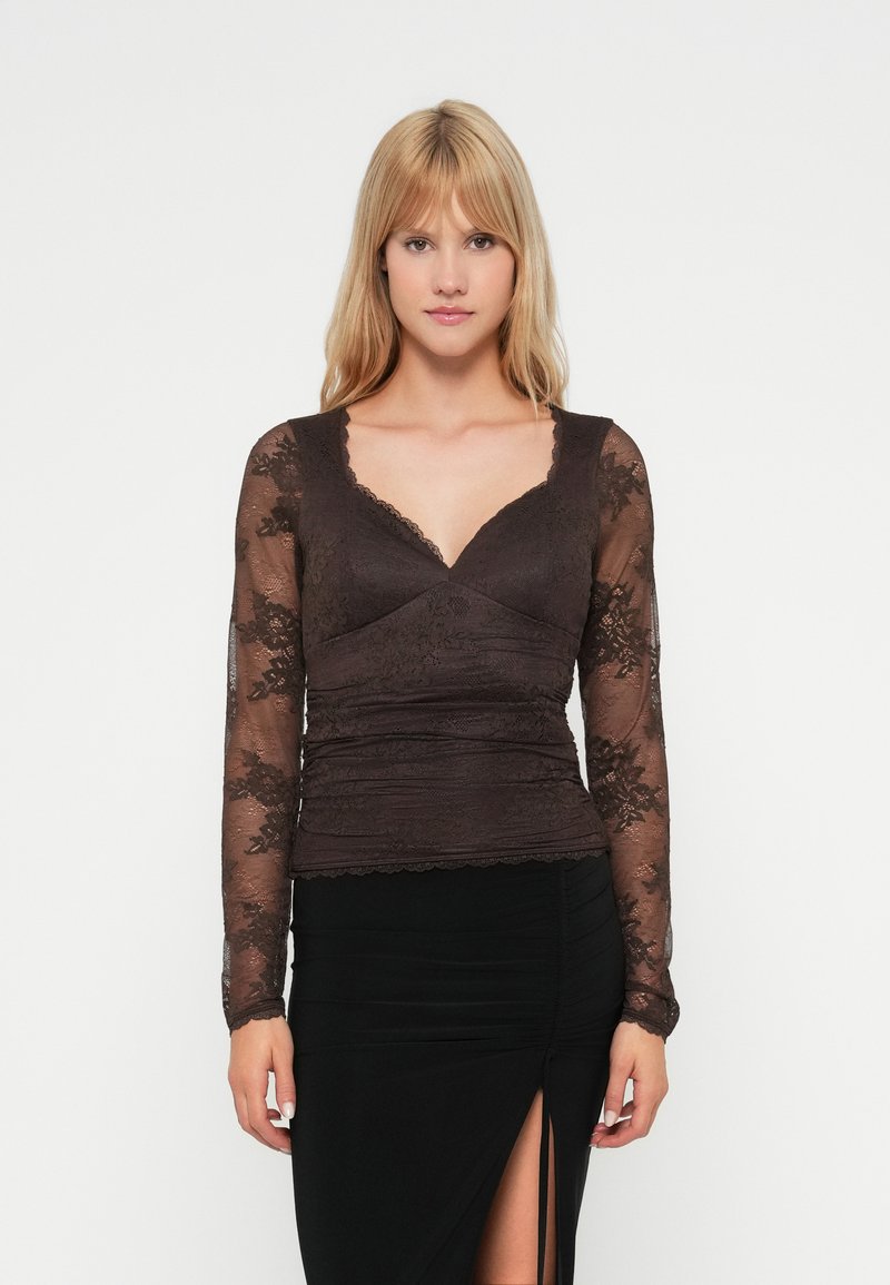 Donkerbruin blouse met lange mouwen en kantdetails, V-hals, getailleerde lijfje en gerimpelde textuur, gecombineerd met een zwarte rok met een zijsplit.