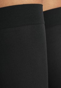 Sorte lårhøje strømper med en blød, ribbet tekstur og et glat elastisk bånd øverst for en sikker pasform. Ingen synlige mønstre eller accenter.