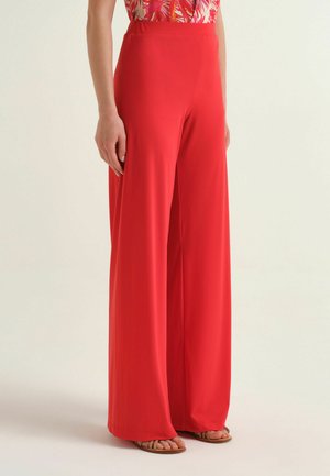 Pantaloni rossi a gamba larga indossati con un top rosa e bianco a fantasia e sandali beige, mostrati dalla vita ai piedi su uno sfondo semplice.