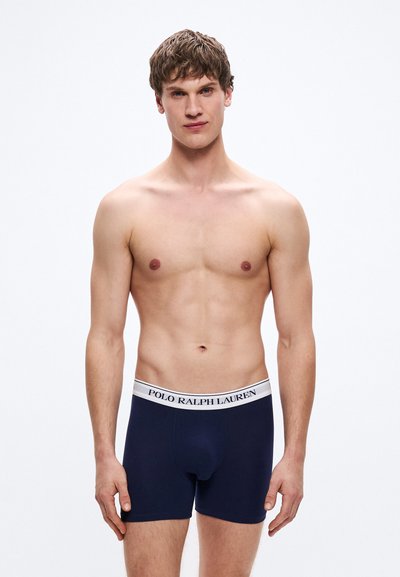 Tmavomodré boxerky s bielym elastickým pásom so značkou „POLO RALPH LAUREN“. Mäkká látka, priliehavý strih, minimálne švy.