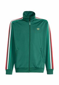 Zelená sportovní bunda na zip s vysokým límcem, má červené, bílé a zelené pruhy podél rukávů a malé zlaté logo na hrudi.