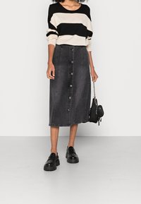 Svart och beige randig tröja i kombination med en grå denim midi kjol med framknappar och sidoklor. Svarta klackskor och handväska.