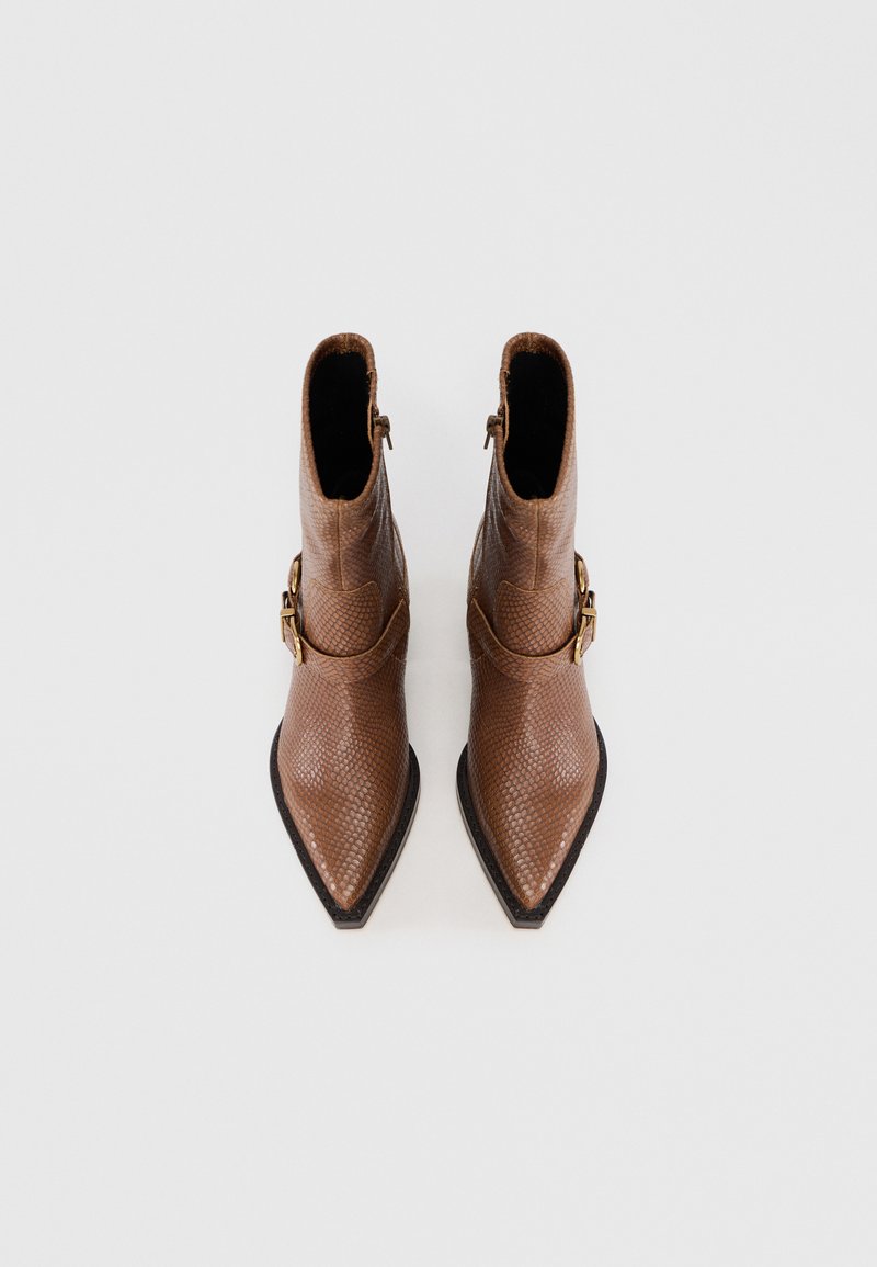 Braune strukturierte Stiefeletten mit spitzem Zehenbereich, seitlichem Reißverschluss und einem dekorativen goldenen Schnallen-Detail am äußeren Knöchel.