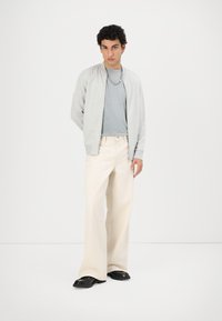 Gray lightweight bomber jacket over a light blue t-shirt, paired with cream wide-leg pants and black shoes. Simple design and neutral colors.