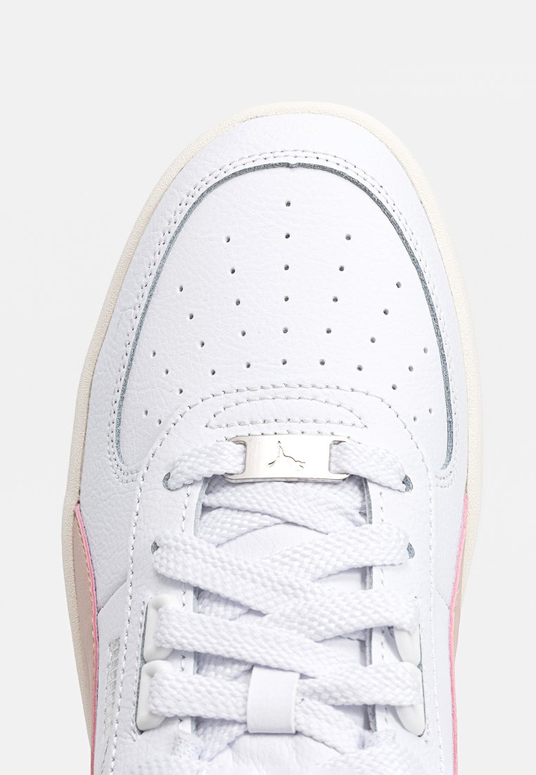 Baskets en cuir blanc avec perforations, lacets blancs, étiquette en métal argenté et bord de semelle beige, présentées en gros plan de dessus.