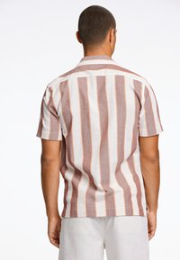 La camisa de manga corta presenta rayas verticales en tonos de marrón rojizo y crema, con un corte relajado y detalle en el yugo trasero.