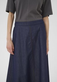 Fustă din denim închis, cu o formă largă și fluidă. Dispune de un tiv drept și de cusături contrastante portocalii pe margini. Material texturat.