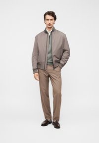 Ανοιχτό γκρι μπουφάν bomber, πράσινο πουλόβερ, μπεζ παντελόνια και καφέ δερμάτινα παπούτσια. Υγρό ύφασμα με μινιμαλιστικό σχεδιασμό και διακριτικές υφές.