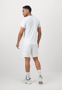 Männer T-Shirt in Weiß, kurzärmelig, kombiniert mit weißen Shorts und Sportschuhen, verfügt über eine glatte Textur und ein einfaches Design.