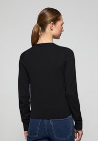 Pull en tricot noir à manches longues, avec un col rond et un ourlet côtelé. Présente une texture lisse et un design ajusté.