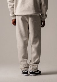 Helle graue Sweatpants mit einer Gesäßtasche, weichem Material, tailliertem Bein Design und getragen mit schwarz-weißen Sneakern.