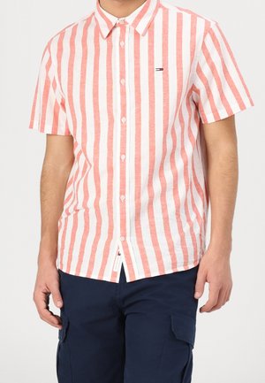 Man wearing short-sleeve shirt with vertical red and white stripes, buttoned front, paired with dark blue cargo pants.