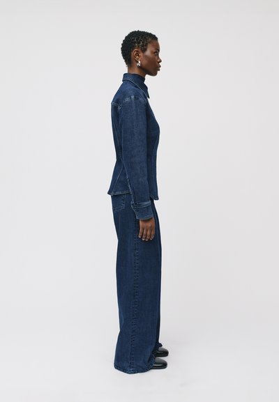 Completo in denim scuro composto da una maglietta aderente con colletto e pantaloni a gamba larga. Il tessuto ha un aspetto strutturato e la silhouette è slanciata.