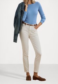 Ljusblå långärmad topp, vita denimjeans, brun bälte och bruna loafers. Denimjacka hängande över armen. Enkelt mönster med avslappnad stil.