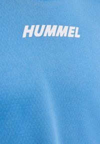 Tissu texturé bleu avec logo HUMMEL blanc centré sur la partie supérieure, probablement un vêtement de sport.