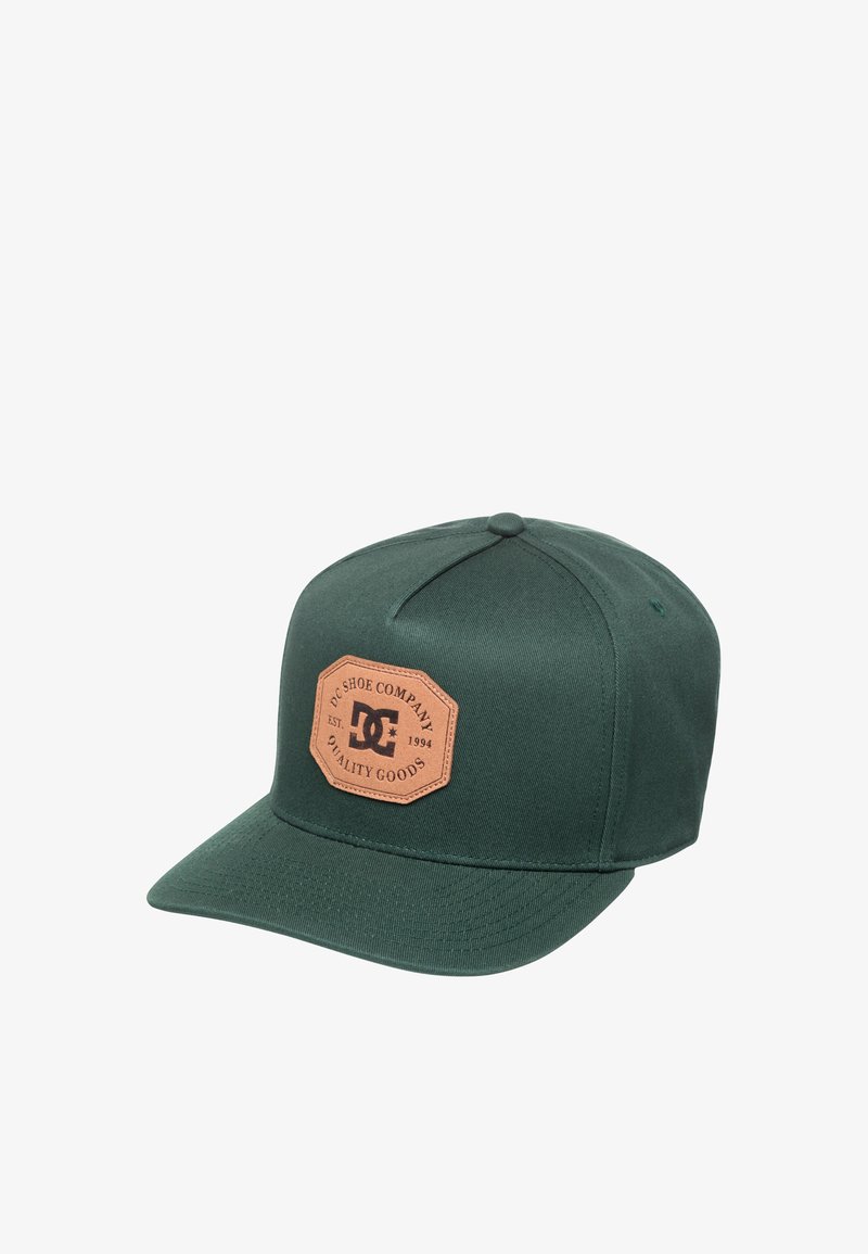 Casquette de baseball vert foncé avec visière plate et logo en patch marron indiquant "DC Shoe Company Est. 1994 Quality Goods" sur le panneau avant.