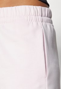 Svetlo roza trenirke s elastično elastiko, stranskimi žepi in mehkobno, teksturirano tkanino. Oblikovanje je preprosto in funkcionalno.