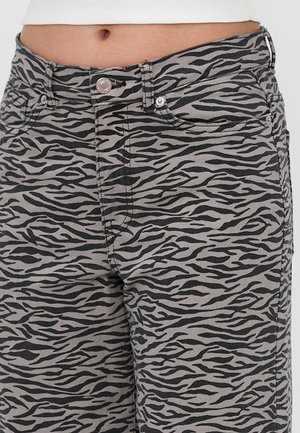 Zbliżenie talii i bioder w szarych spodniach z czarnym wzorem tygrysich pasków i białym topie.