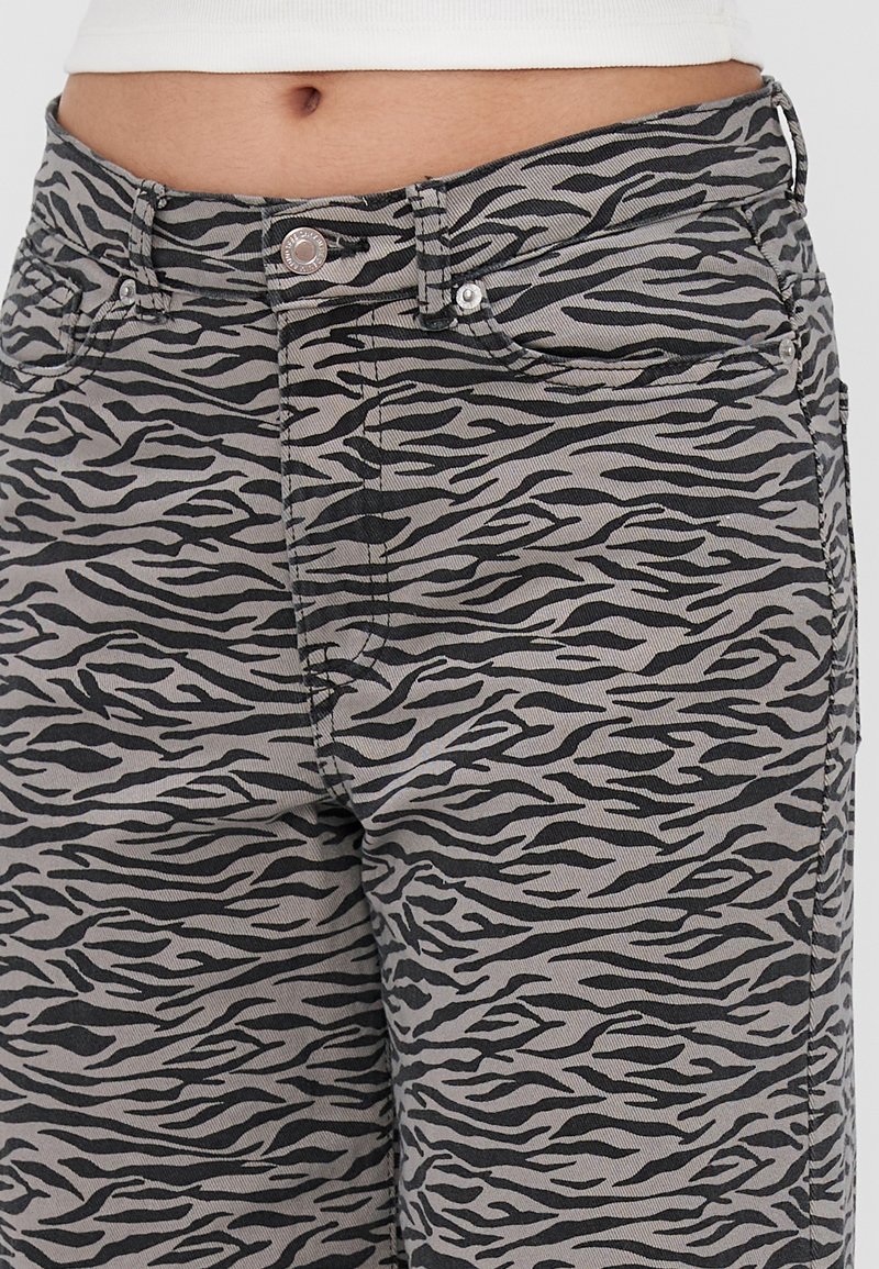 Gros plan sur la taille et les hanches portant un pantalon gris avec un motif rayures de tigre noir et un haut blanc.