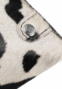 Cowhide wallet featuring a black and white spotted pattern, with a silver snap button and textured surface. Edge stitching visible.
