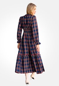 Largo vestido de cuadros en azul oscuro, con un estampado de cuadros en rojo y verde, mangas abullonadas, cintura elástica y un dobladillo con volantes en capas.