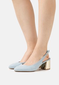 Talons slingback en daim bleu clair avec un bout arrondi et un talon bloc métallique doré. Comprend une bride avec une boucle dorée.