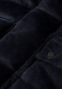 Gilet imbottito blu navy realizzato in tessuto testurizzato, con sezioni trapuntate e un bottone a pressione nero rotondo. La vista ravvicinata mette in evidenza i dettagli del tessuto.