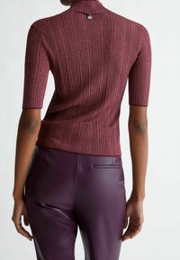 Viininpunainen ribbineulottu paita, jossa on lyhyet hihat ja korkea kaulus, selkäpuolella nappi. Yhdistetty tummanvioletteihin nahkahousuihin.