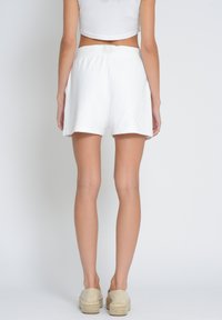 White cotton shorts with a relaxed fit and elastic waistband, featuring a subtle embroidered accent. Smooth texture, mid-thigh length.