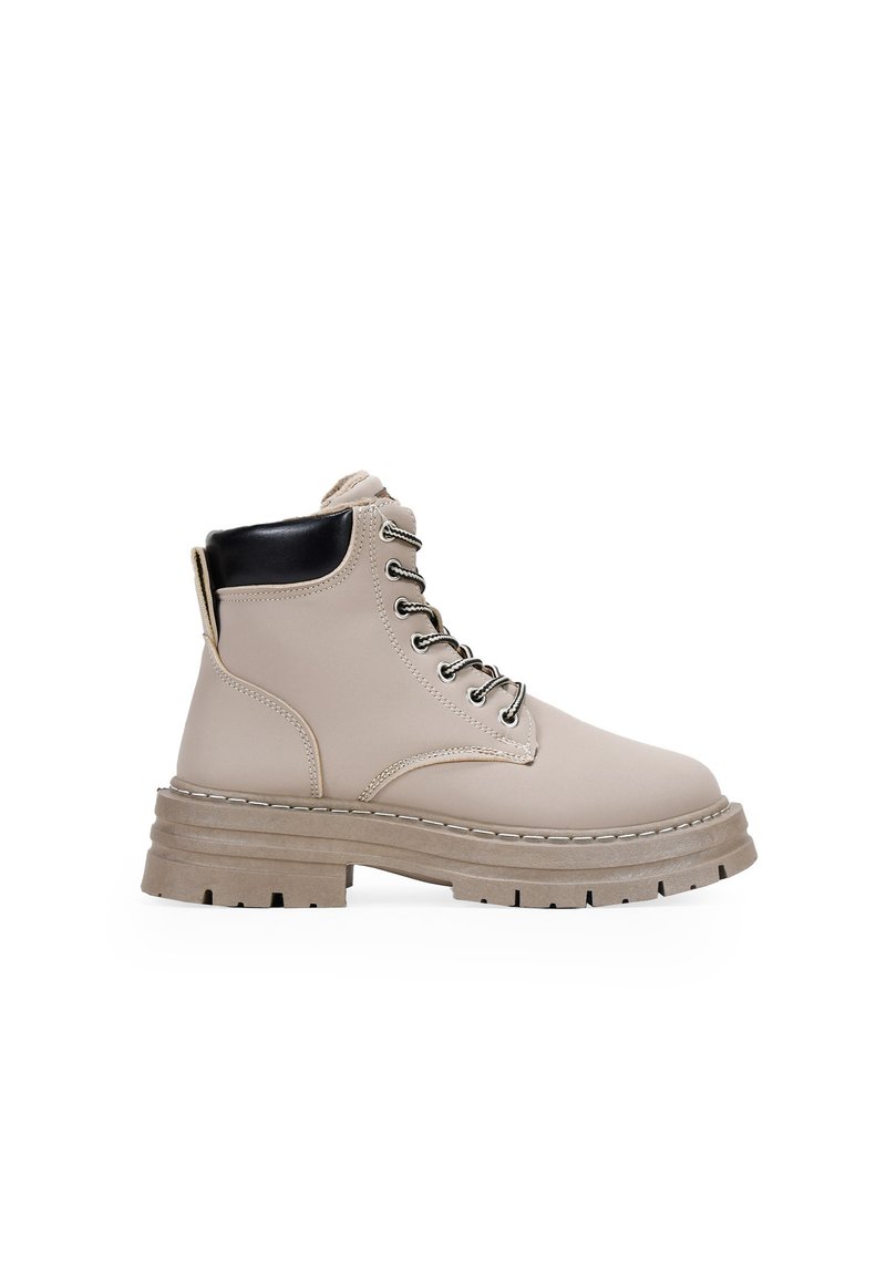 Bottines beiges à lacets avec une finition texturée, accent de talon noir et semelle épaisse avec des crampons profonds pour une meilleure adhérence. Quincaillerie en argent incluse.