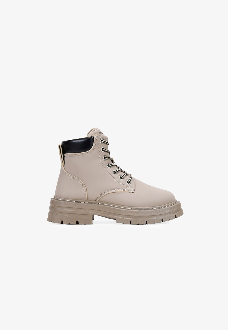 Bottines beiges à lacets avec une finition texturée, accent de talon noir et semelle épaisse avec des crampons profonds pour une meilleure adhérence. Quincaillerie en argent incluse.