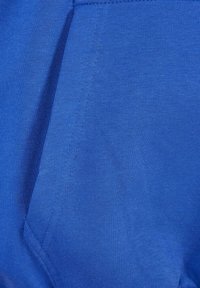 Tela de algodón azul con textura suave, que presenta un detalle de bolsillo y un ligero acanalado a lo largo de las costuras. El color es uniforme en toda la tela.