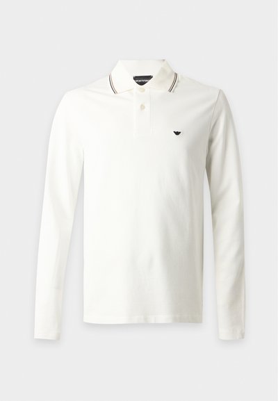 Polo blanc à manches longues avec un col présentant des rayures noires et beiges et un petit logo noir sur la poitrine gauche.