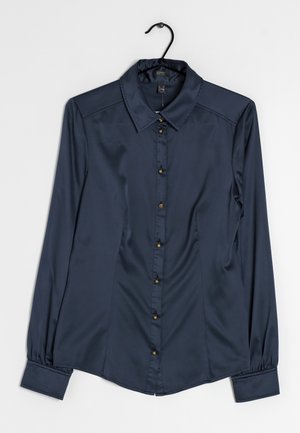 Chemise en satin bleu marine à manches longues avec col pointu et boutons dorés, suspendue sur un cintre noir sur fond blanc.