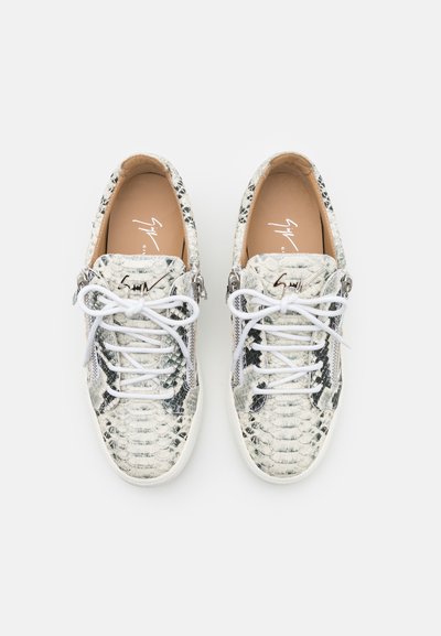 Baskets en imprimé serpent noir et blanc avec une surface texturée, dotées de lacets blancs et de zips sur les côtés, sur une semelle blanche.