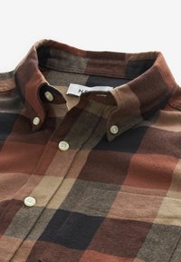 Chemise en flanelle à col boutonné avec un grand motif à carreaux marron, beige et noir et boutons couleur crème, pliée à plat.