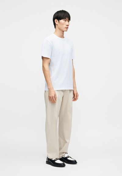 Λευκό βαμβακερό t-shirt, άνετη γραμμή, κοντά μανίκια. Συνδυασμένο με ανοιχτό μπεζ παντελόνι και μαύρα και λευκά μοκασίνια με χρυσές λεπτομέρειες.