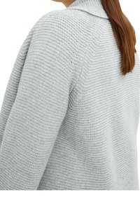 Cardigan lavorato a maglia grigio chiaro con un motivo testurizzato, maniche lunghe e colletto. Il filato sembra morbido e densamente tessuto.