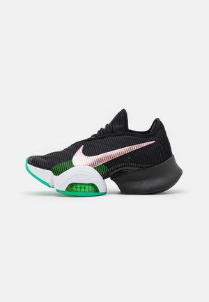 Chaussure de sport noire avec un swoosh Nike rose, des accents verts, et une semelle unique en deux sections avec un amorti à air visible sous l'avant-pied.