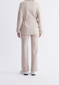 Beige stickad topp med bälte i midjan, kombinerad med matchande vida byxor. Skorna är vita med svarta stjärndetaljer. Mjuk textur, avslappnad passform.