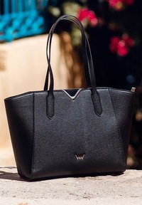 Černá taška přes rameno vyrobená z texturovaného syntetického materiálu s dvěma pevnými uchy, V-tvarovaným akcentem a jemným logem na přední straně.