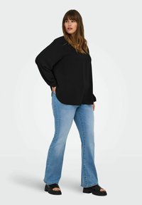 Crna majica dugih rukava opuštenog kroja, uparena sa svijetloplavim trapericama s razduženim nogavicama. Model nosi crne platforme s debelim potplatom.